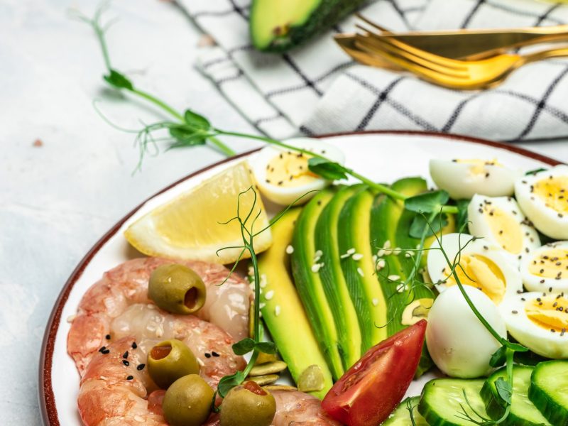 Ketogenic breakfast. Keto low carb shrimps, prawns, quail eggs, fresh salad, tomatoes, cucumbers and avocado on a light background. keto diet. Top view,